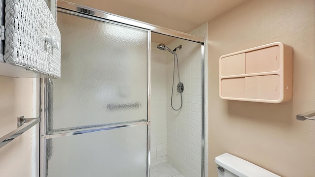 bathroom featuring a shower with door and toilet