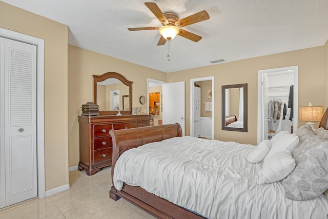 bedroom featuring ceiling fan, a textured ceiling, light tile patterned floors, and ensuite bathroom