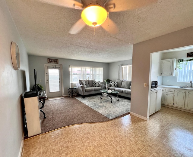 living room featuring a ceiling fan, baseboards, a textured ceiling, and light floors