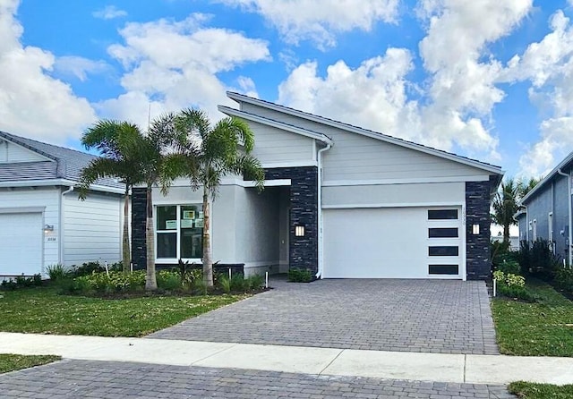 view of front of home with a garage, stone siding, decorative driveway, and a front yard