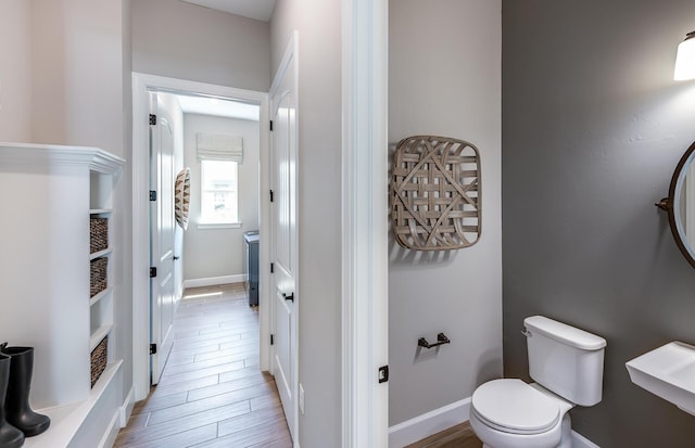 half bathroom with baseboards, toilet, and wood finished floors