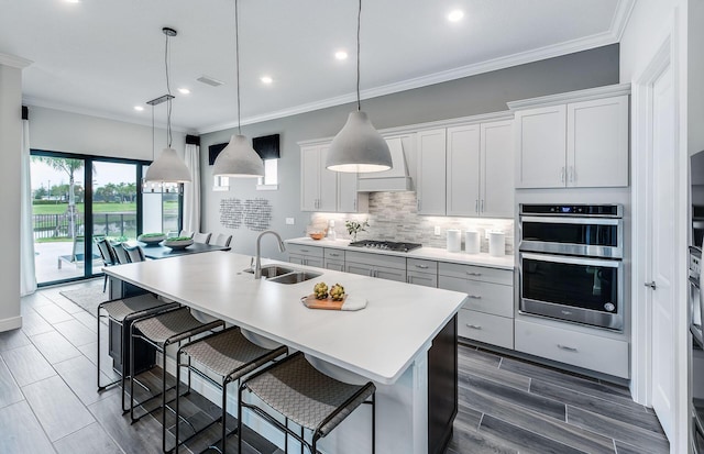 kitchen featuring appliances with stainless steel finishes, decorative light fixtures, sink, white cabinets, and a center island with sink