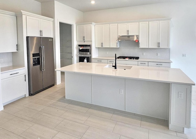 kitchen featuring stainless steel appliances, tasteful backsplash, white cabinets, a sink, and under cabinet range hood