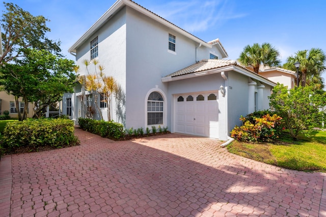 view of front of house with an attached garage, decorative driveway, stucco siding, and a tiled roof