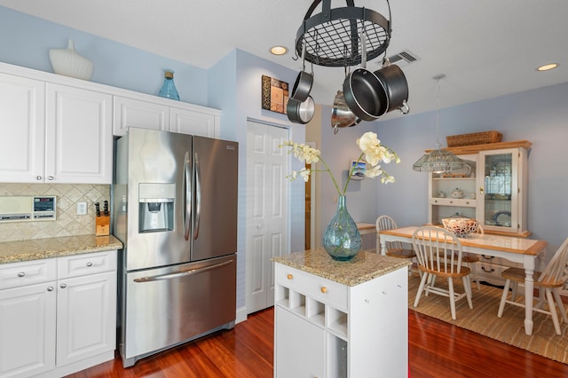 kitchen with stainless steel fridge, white cabinets, light stone counters, and dark hardwood / wood-style floors