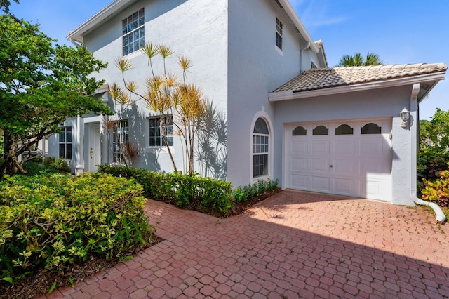 view of side of property with stucco siding, a garage, decorative driveway, and a tiled roof
