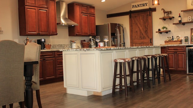 kitchen with light stone countertops, wall chimney exhaust hood, a breakfast bar, vaulted ceiling, and a kitchen island with sink