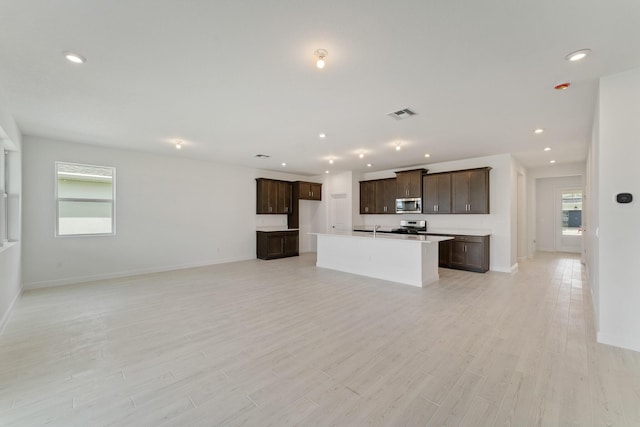 kitchen featuring appliances with stainless steel finishes, sink, light hardwood / wood-style floors, dark brown cabinets, and a center island with sink