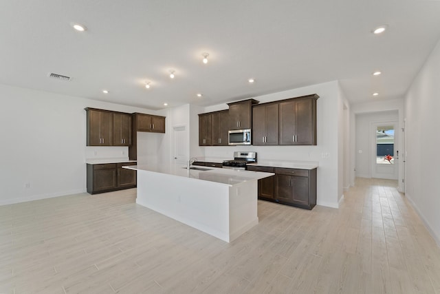 kitchen featuring light hardwood / wood-style flooring, dark brown cabinets, stainless steel appliances, and a center island with sink