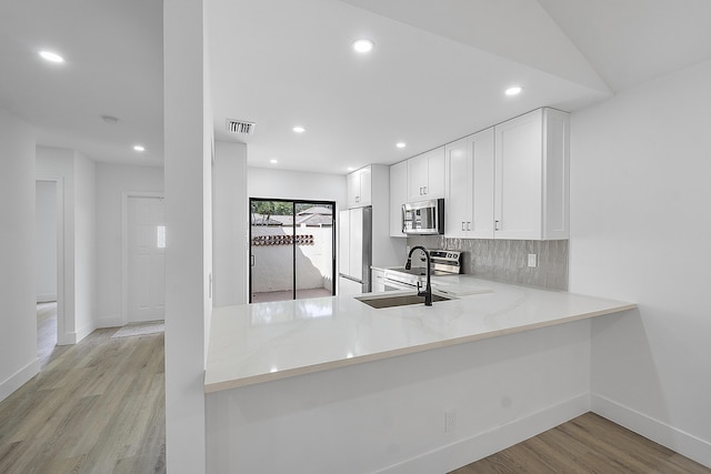 kitchen with sink, white cabinetry, stainless steel appliances, kitchen peninsula, and light wood-type flooring