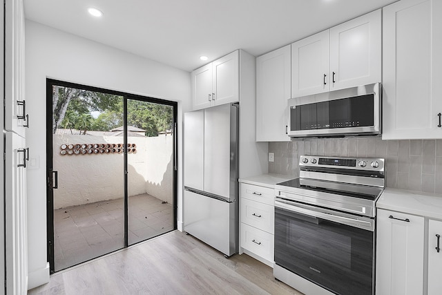 kitchen with appliances with stainless steel finishes, white cabinets, backsplash, light stone countertops, and light hardwood / wood-style flooring