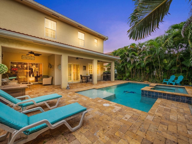 pool at dusk featuring ceiling fan, an in ground hot tub, and a patio