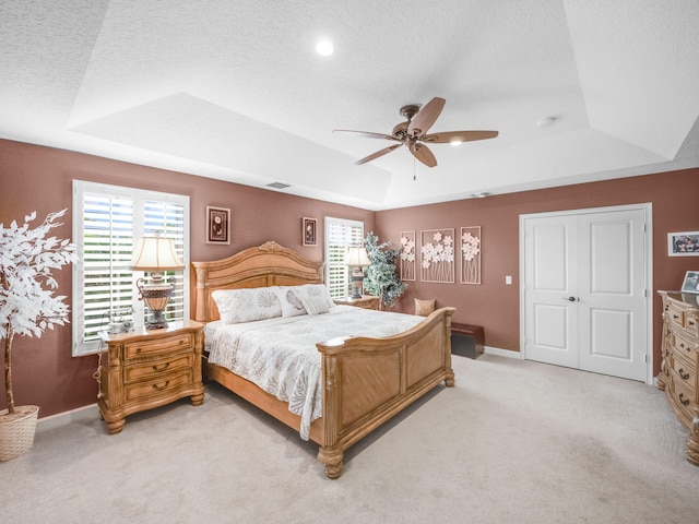 bedroom featuring a textured ceiling, ceiling fan, light carpet, and a tray ceiling