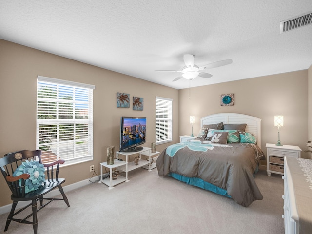 bedroom featuring a textured ceiling, light colored carpet, multiple windows, and ceiling fan