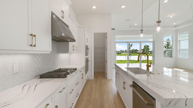 kitchen featuring white cabinets, pendant lighting, sink, stainless steel appliances, and light wood-type flooring