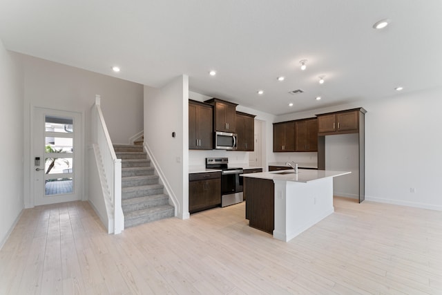 kitchen featuring appliances with stainless steel finishes, dark brown cabinets, sink, a center island with sink, and light hardwood / wood-style flooring