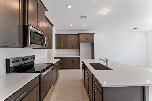 kitchen with dark brown cabinets, sink, stainless steel appliances, and light hardwood / wood-style flooring