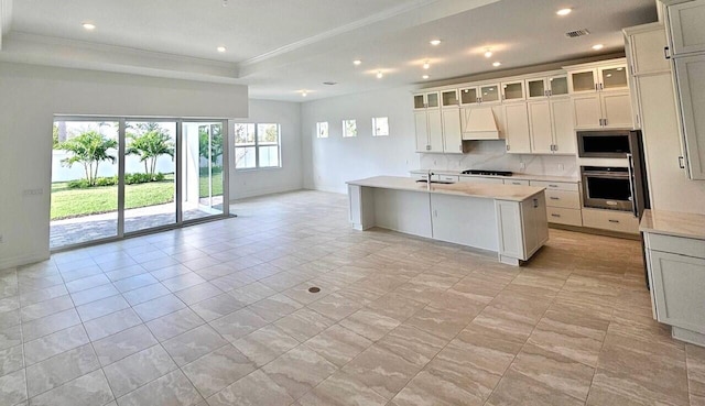 kitchen with custom range hood, stainless steel appliances, crown molding, sink, and a center island with sink