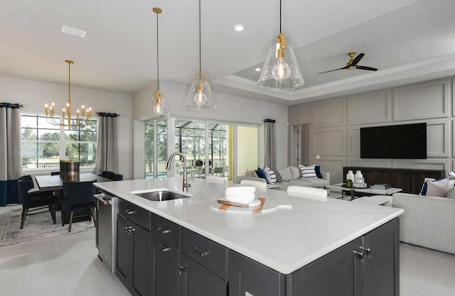 kitchen with pendant lighting, ceiling fan with notable chandelier, a center island with sink, and sink