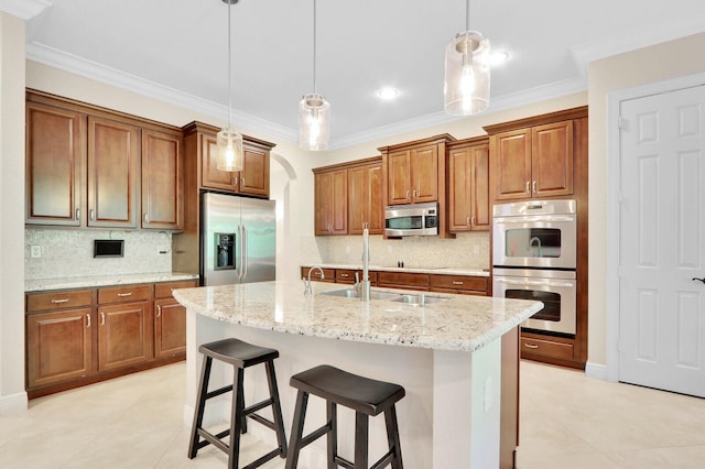 kitchen featuring appliances with stainless steel finishes, decorative light fixtures, light stone counters, a breakfast bar, and a center island with sink