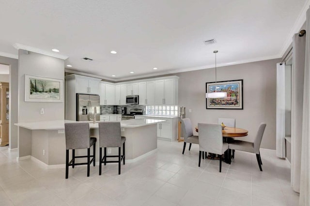 kitchen with pendant lighting, a kitchen island, ornamental molding, appliances with stainless steel finishes, and white cabinetry