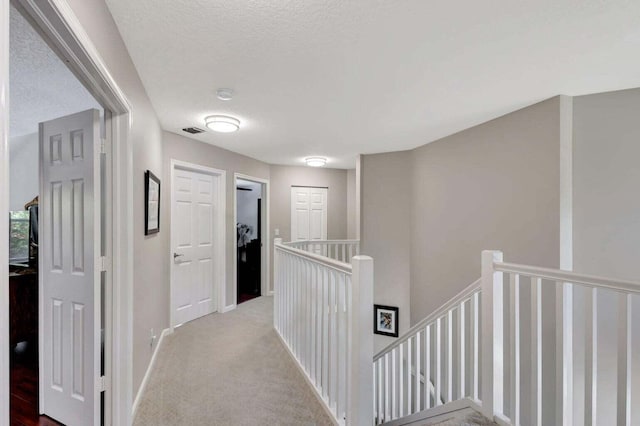 hallway with a textured ceiling and light colored carpet