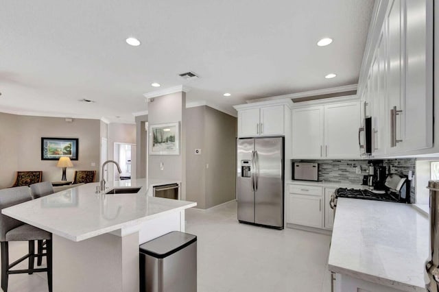 kitchen with tasteful backsplash, a center island with sink, sink, appliances with stainless steel finishes, and white cabinetry