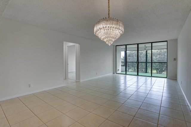 empty room featuring a wall of windows, a notable chandelier, light tile patterned floors, and a textured ceiling