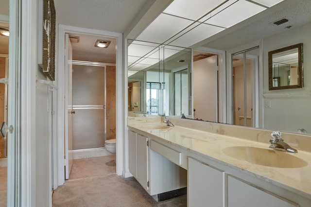 bathroom with vanity, a shower with shower door, toilet, and a textured ceiling