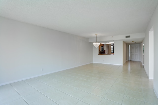 tiled empty room with an inviting chandelier and a textured ceiling