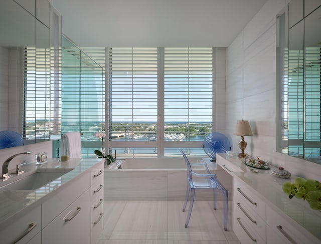 bathroom with tile patterned floors, vanity, a relaxing tiled tub, and a water view