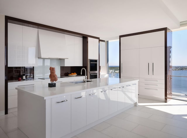 kitchen with decorative backsplash, white cabinetry, sink, and an island with sink