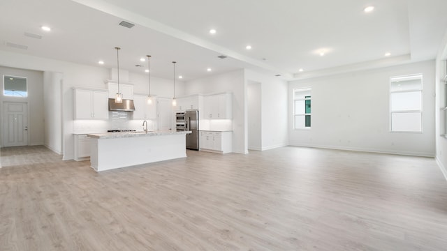 kitchen featuring an island with sink, stainless steel appliances, light hardwood / wood-style floors, hanging light fixtures, and white cabinetry