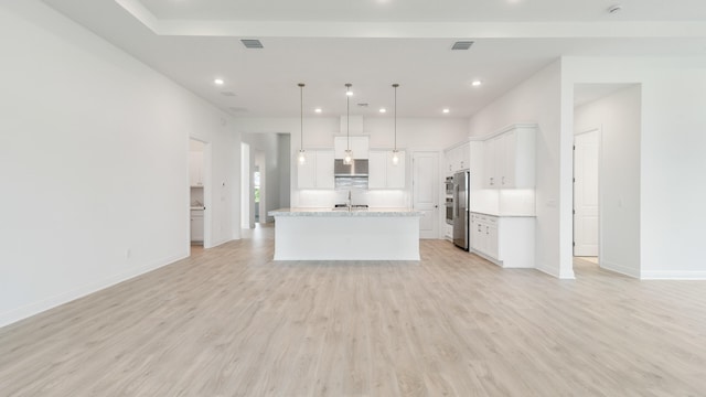 kitchen featuring pendant lighting, an island with sink, white cabinets, and stainless steel fridge