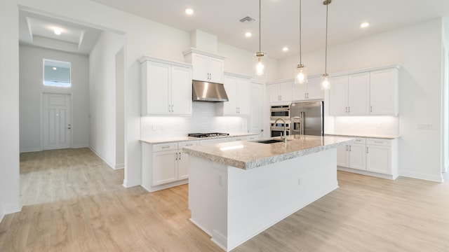 kitchen featuring an island with sink, light wood-type flooring, hanging light fixtures, white cabinetry, and appliances with stainless steel finishes