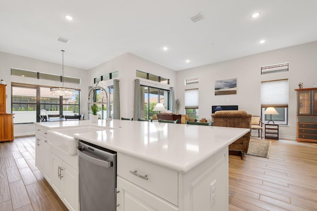 kitchen with a wealth of natural light, hanging light fixtures, a kitchen island with sink, and stainless steel dishwasher