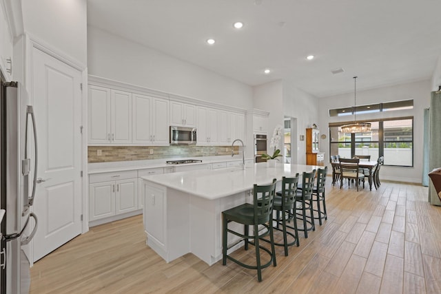 kitchen featuring pendant lighting, white cabinetry, light hardwood / wood-style flooring, appliances with stainless steel finishes, and a center island with sink