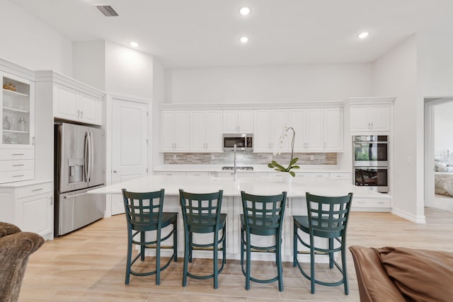 kitchen featuring light hardwood / wood-style floors, appliances with stainless steel finishes, a kitchen bar, and white cabinetry