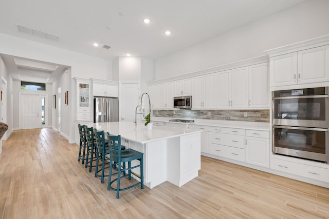 kitchen featuring white cabinets, appliances with stainless steel finishes, light wood-type flooring, and a kitchen island with sink