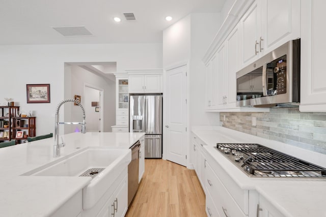 kitchen with tasteful backsplash, sink, light hardwood / wood-style floors, white cabinetry, and appliances with stainless steel finishes