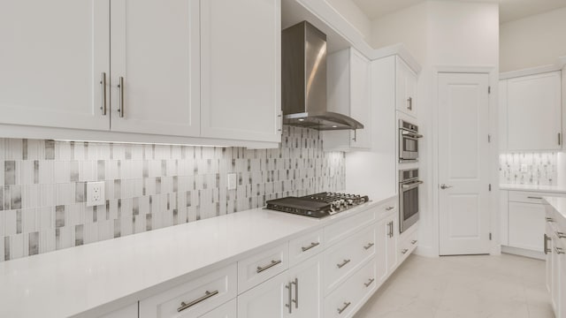 kitchen featuring backsplash, wall chimney range hood, stainless steel gas cooktop, and white cabinets