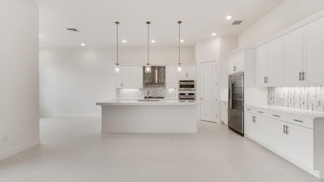 kitchen with wall chimney range hood, a center island with sink, hanging light fixtures, white cabinets, and appliances with stainless steel finishes