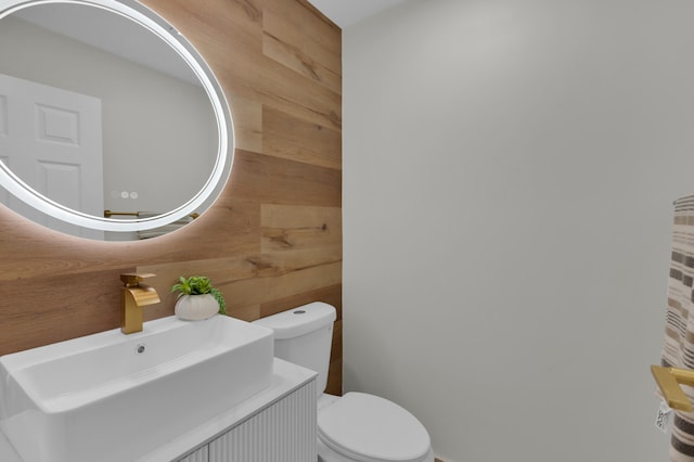 bathroom with vanity, wooden walls, and toilet