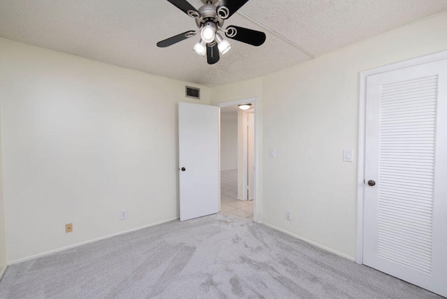 unfurnished bedroom with a closet, light colored carpet, a textured ceiling, and ceiling fan