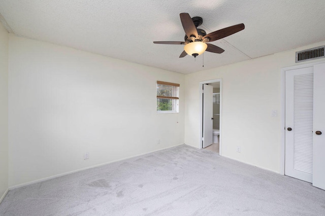 unfurnished bedroom with ceiling fan, light colored carpet, a closet, ensuite bath, and a textured ceiling