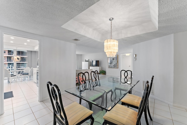 tiled dining room with a textured ceiling, an inviting chandelier, and a tray ceiling