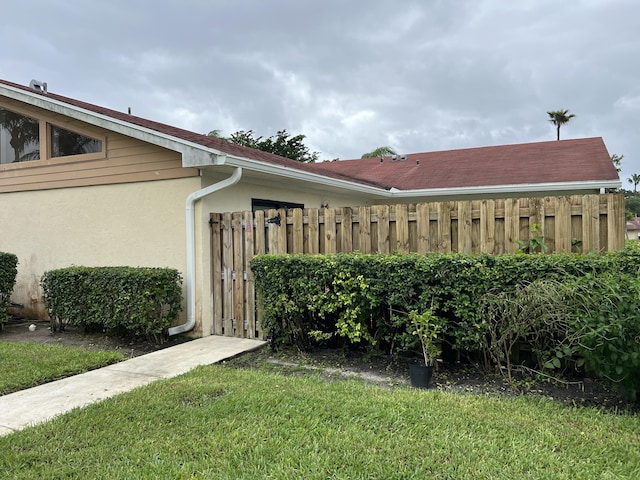 view of property exterior with stucco siding, fence, and a lawn