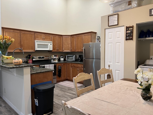 kitchen featuring wood finished floors, brown cabinets, a towering ceiling, a peninsula, and appliances with stainless steel finishes