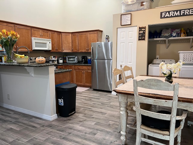 kitchen featuring stainless steel refrigerator, washing machine and clothes dryer, hardwood / wood-style floors, a breakfast bar, and dark stone countertops