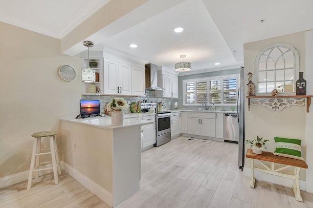 kitchen featuring kitchen peninsula, wall chimney exhaust hood, stainless steel appliances, pendant lighting, and white cabinets